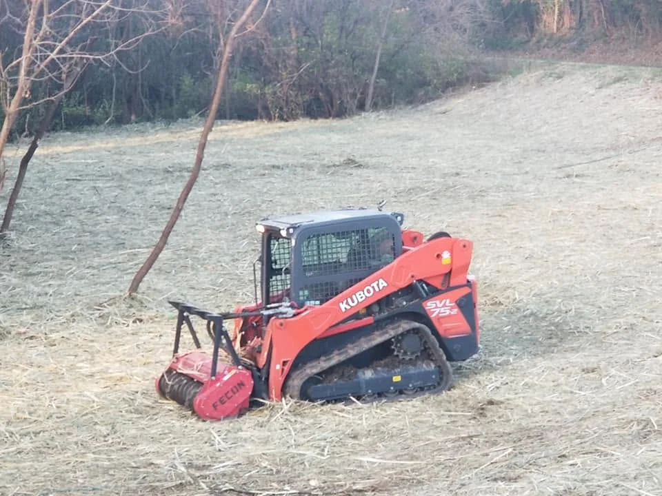 Kubota skid steer with a FEcon brush cutter clearing a grassy rural property